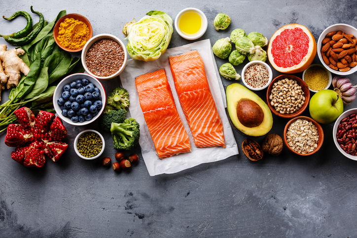 Fish surrounded by vegetables, fruit, nuts, and other healthy food choices